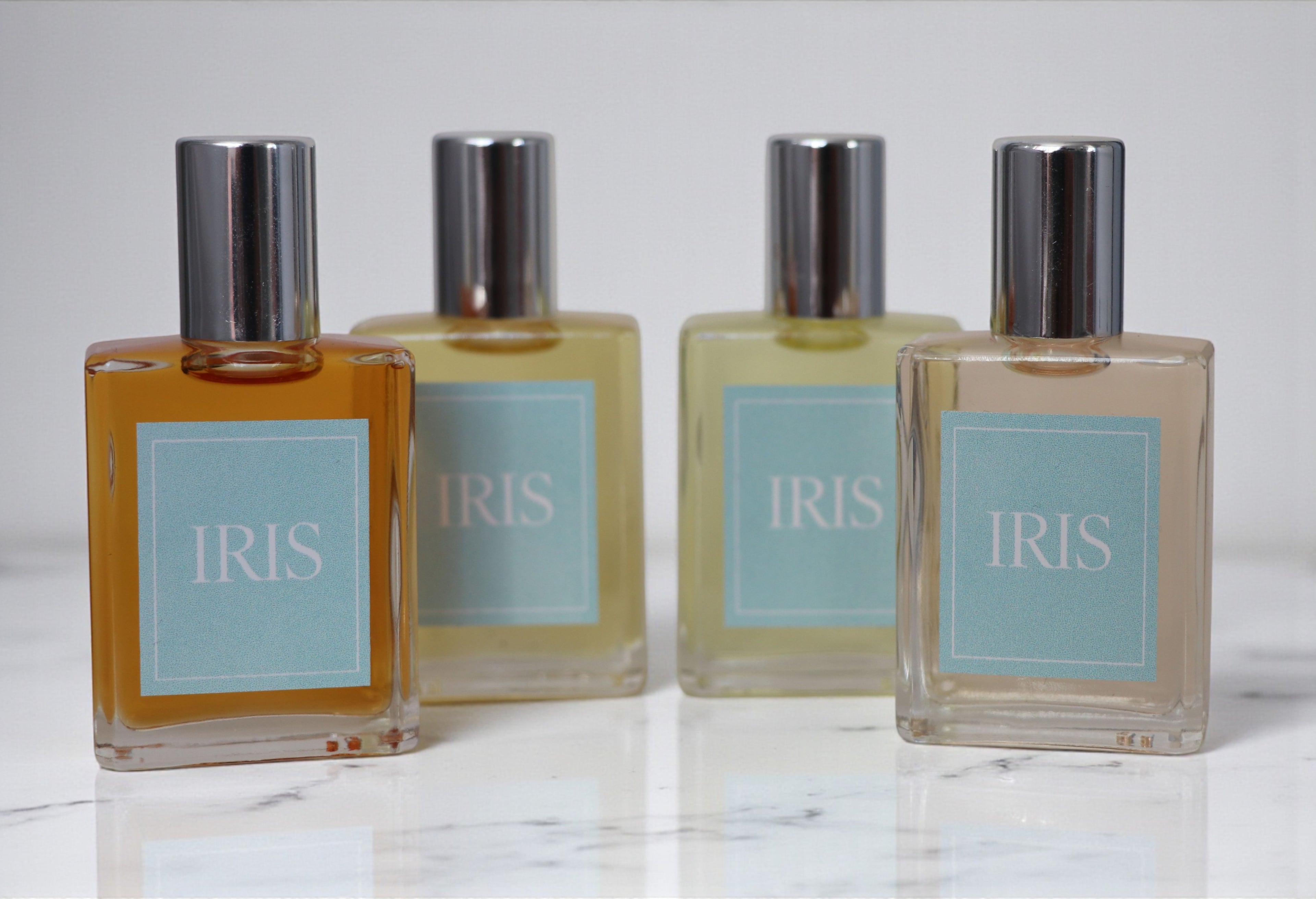 Four bottles of Iris perfume on a marble surface with a light gray background